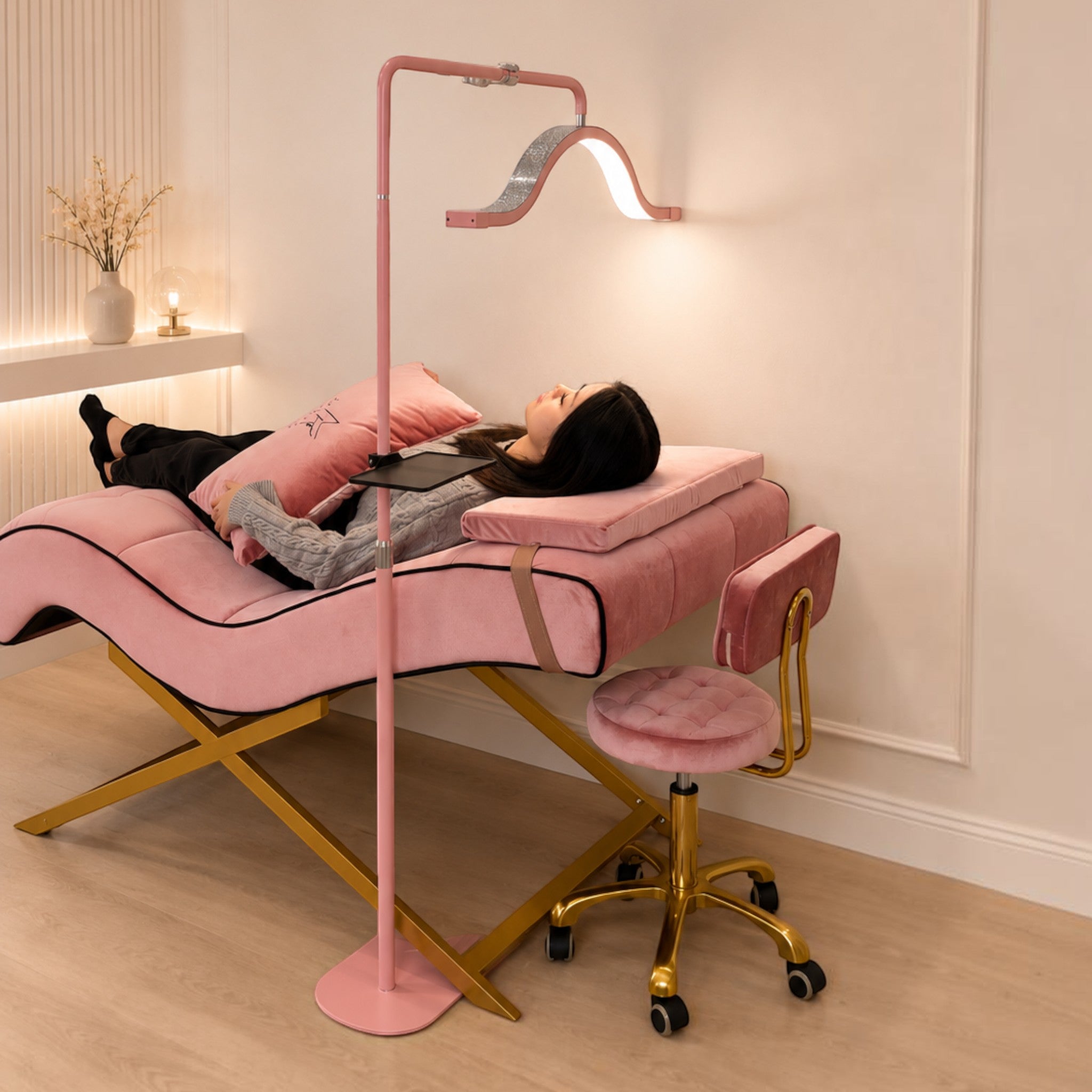 MK BEAUTY BED pink velvet curved treatment bed with gold X-cross base and matching stool in a modern salon setting