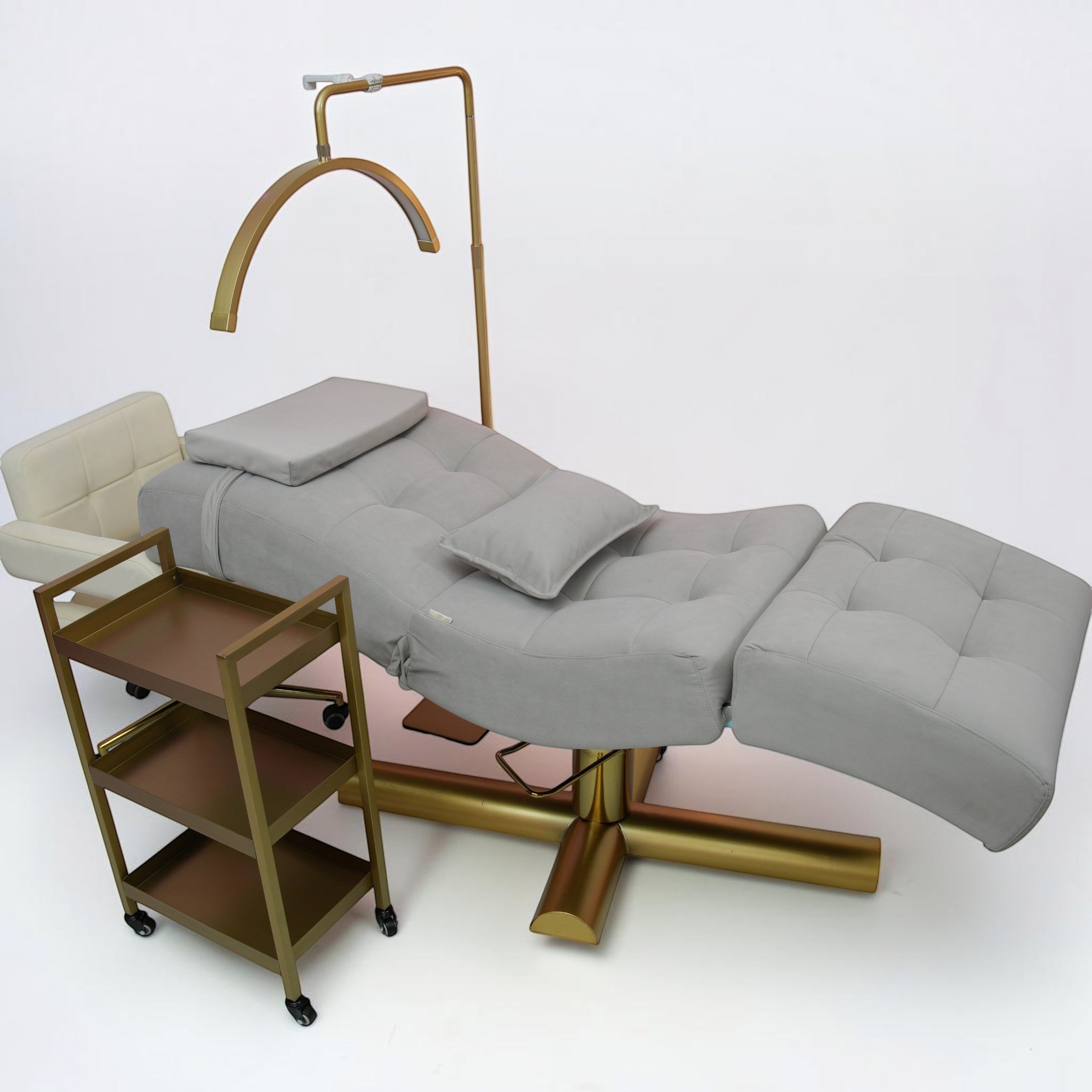MK BEAUTY BED All in One Curved Bed in grey with gold hydraulic base, matching trolley, and overhead salon light.