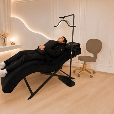 MK BEAUTY BED All in One Curved Bed in black with an X-Cross base, featuring a client receiving a treatment.