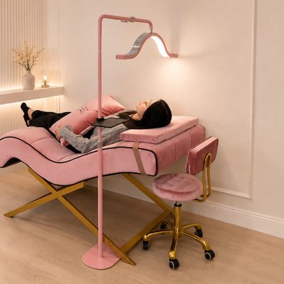 MK BEAUTY BED pink velvet curved treatment bed with gold X-cross base and matching stool in a modern salon setting